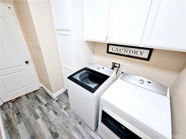 clothes washing area with cabinets, washing machine and clothes dryer, and light hardwood / wood-style flooring