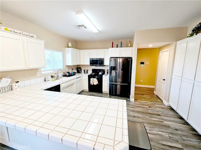 kitchen featuring sink, white cabinetry, tile countertops, light wood-type flooring, and black appliances