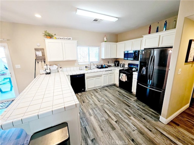 kitchen featuring sink, light hardwood / wood-style flooring, black appliances, white cabinets, and tile countertops