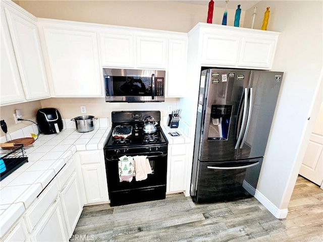 kitchen with white cabinetry, stainless steel appliances, tile countertops, and light hardwood / wood-style floors