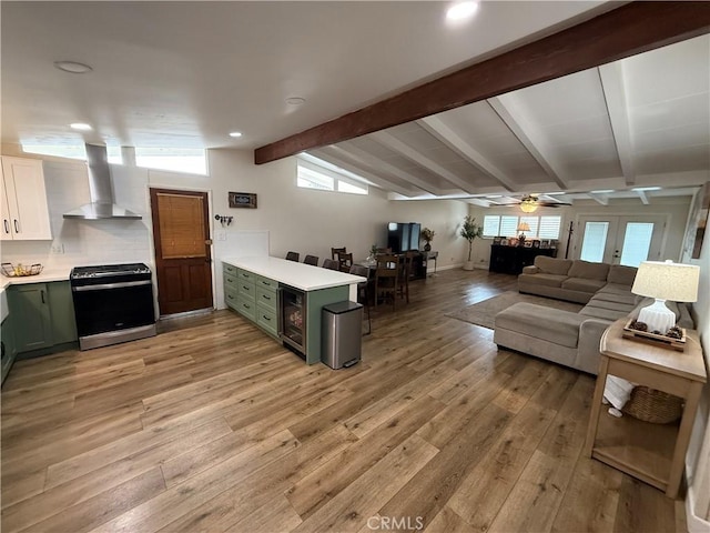 kitchen with light wood-style floors, gas stove, wall chimney range hood, and green cabinetry