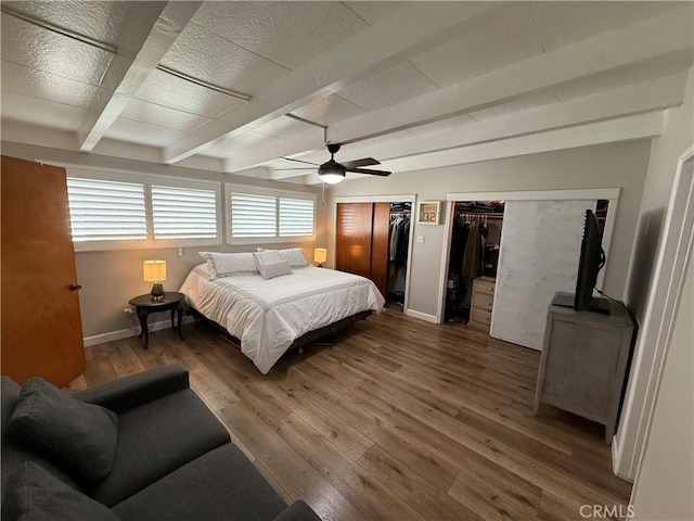 bedroom with multiple closets, ceiling fan, dark wood-type flooring, and beamed ceiling