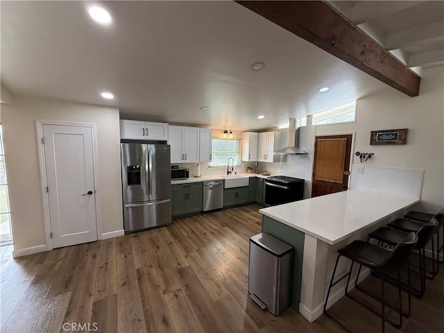 kitchen featuring wood finished floors, wall chimney exhaust hood, a peninsula, and stainless steel appliances