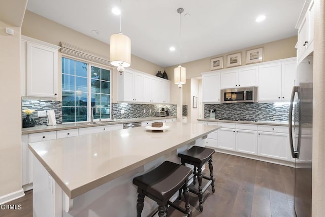 kitchen featuring a kitchen island, appliances with stainless steel finishes, pendant lighting, white cabinets, and dark wood-type flooring