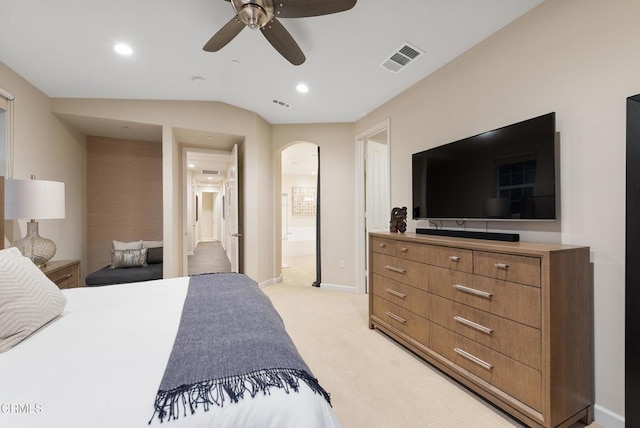 bedroom with ceiling fan, light colored carpet, vaulted ceiling, and ensuite bath