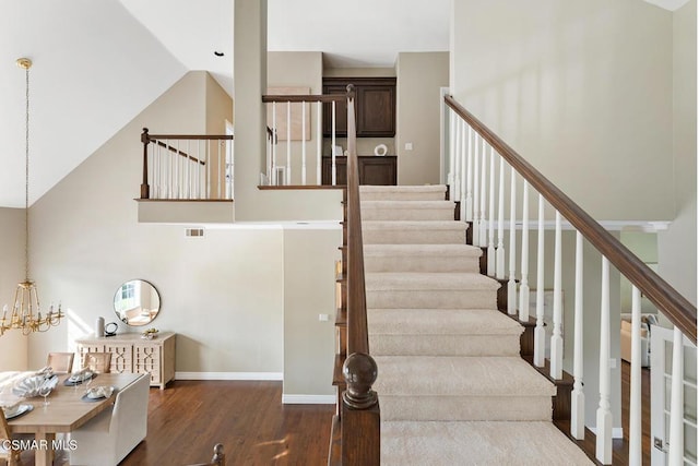 stairway with high vaulted ceiling, hardwood / wood-style floors, and a chandelier