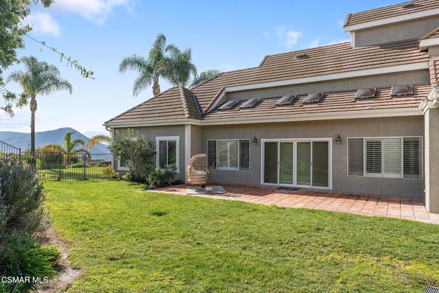 rear view of house featuring a mountain view, a patio, and a lawn