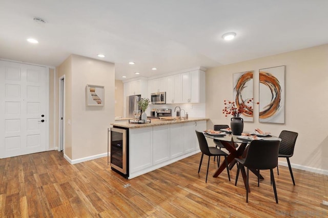 kitchen with white cabinetry, light wood-type flooring, beverage cooler, and appliances with stainless steel finishes