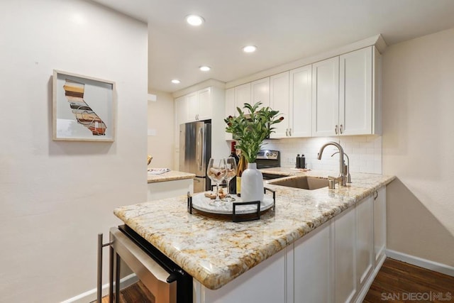 kitchen featuring white cabinetry, sink, backsplash, stainless steel fridge, and light stone counters