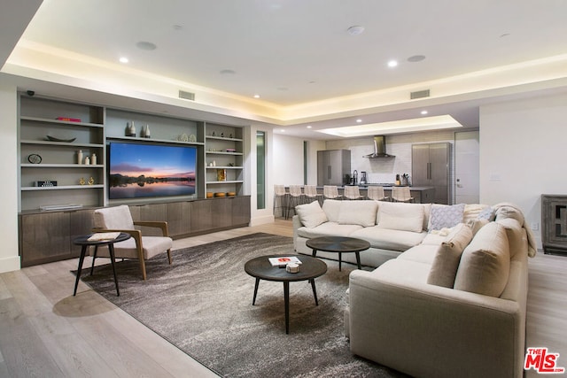 living room featuring a tray ceiling, light hardwood / wood-style flooring, and built in shelves