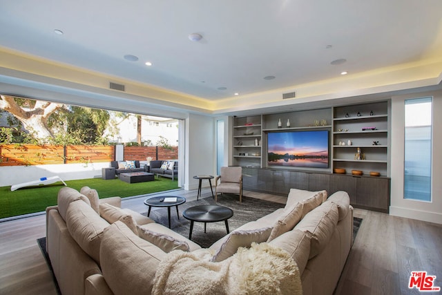 living room with a raised ceiling, hardwood / wood-style floors, and built in shelves