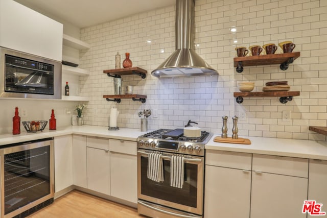 kitchen with tasteful backsplash, wine cooler, gas stove, wall chimney range hood, and light wood-type flooring