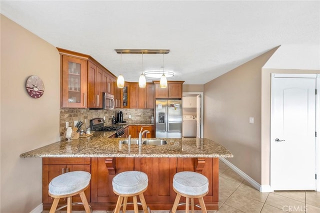 kitchen with kitchen peninsula, decorative light fixtures, sink, washer / clothes dryer, and appliances with stainless steel finishes