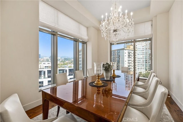 dining area with a notable chandelier, dark wood-type flooring, and a raised ceiling