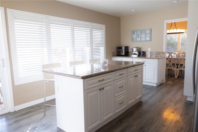 kitchen featuring white cabinetry, a kitchen island, dark wood-type flooring, and a breakfast bar