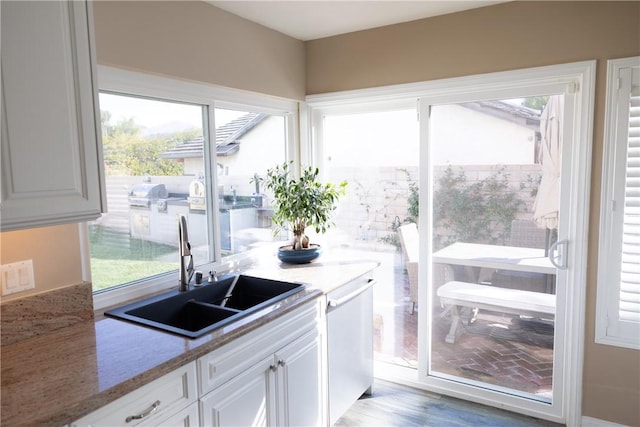 kitchen featuring white cabinetry, sink, light hardwood / wood-style flooring, and stone counters