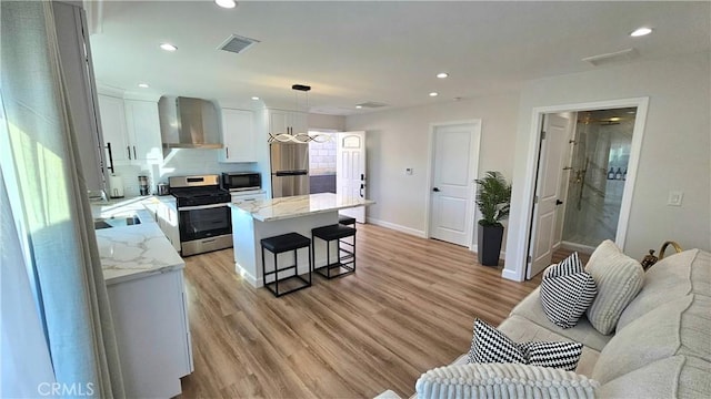 kitchen featuring appliances with stainless steel finishes, white cabinets, a kitchen island, decorative light fixtures, and wall chimney exhaust hood