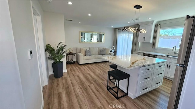 kitchen featuring a kitchen island, sink, stainless steel fridge, white cabinets, and a kitchen breakfast bar