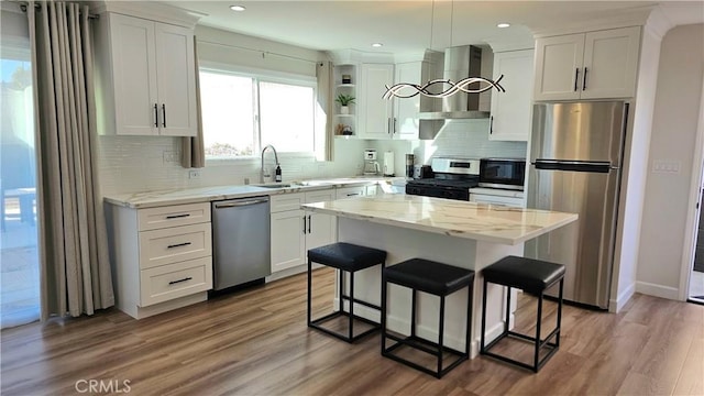 kitchen with a kitchen island, decorative light fixtures, white cabinetry, stainless steel appliances, and wall chimney exhaust hood