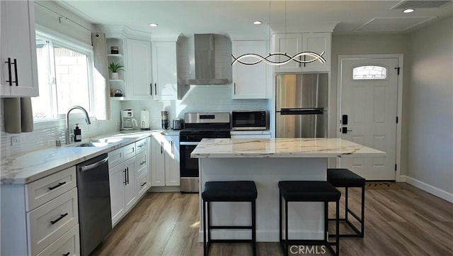 kitchen with white cabinets, a kitchen island, wall chimney exhaust hood, and appliances with stainless steel finishes