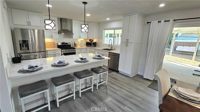 kitchen with sink, hanging light fixtures, appliances with stainless steel finishes, wall chimney range hood, and white cabinets