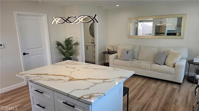 kitchen featuring sink, pendant lighting, white cabinetry, hardwood / wood-style flooring, and light stone countertops