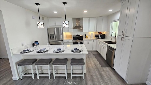 kitchen with appliances with stainless steel finishes, sink, a breakfast bar area, white cabinets, and wall chimney exhaust hood