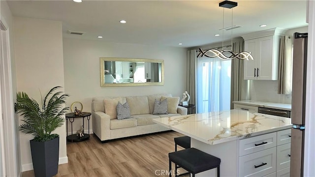 kitchen featuring a breakfast bar, light stone counters, hanging light fixtures, light wood-type flooring, and white cabinets