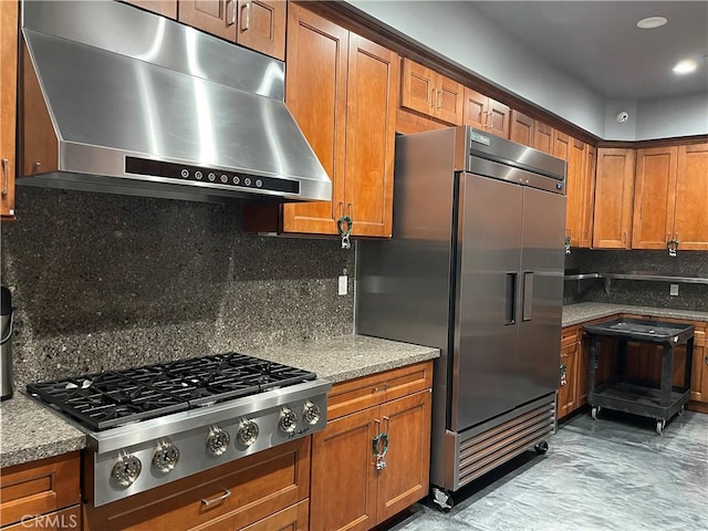 kitchen with appliances with stainless steel finishes, range hood, brown cabinets, and light stone countertops