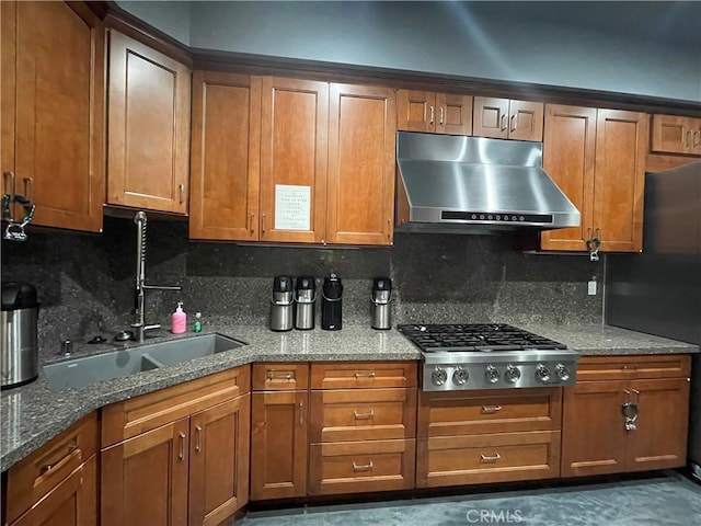 kitchen featuring dark stone counters, appliances with stainless steel finishes, brown cabinetry, and exhaust hood