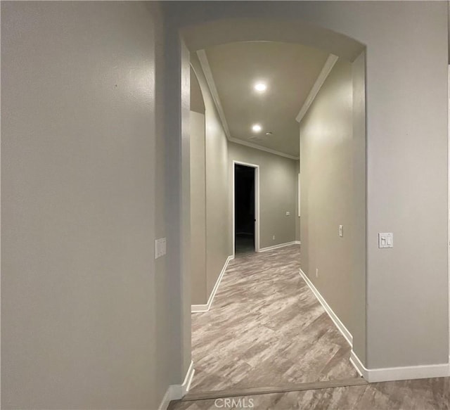 hall with arched walkways, light wood-style flooring, and baseboards