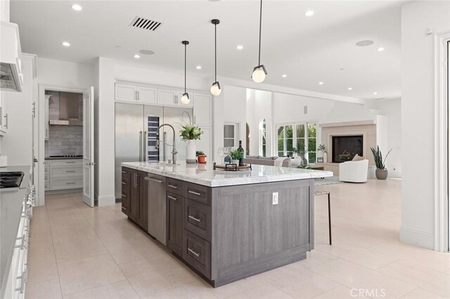 kitchen featuring decorative light fixtures, white cabinetry, a kitchen island with sink, light stone counters, and dark brown cabinets