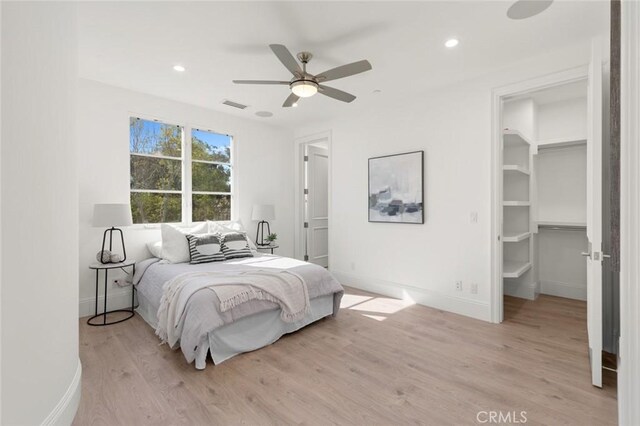 bedroom featuring a walk in closet, ceiling fan, and light hardwood / wood-style flooring