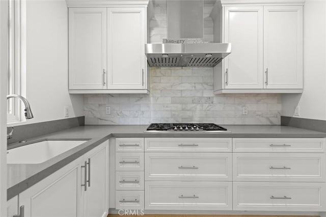 kitchen featuring wall chimney range hood, sink, backsplash, white cabinets, and stainless steel gas stovetop