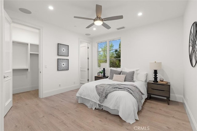 bedroom with ceiling fan, a walk in closet, light wood-type flooring, and a closet