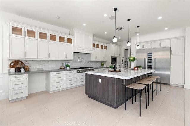 kitchen featuring white cabinets, a kitchen breakfast bar, hanging light fixtures, built in appliances, and a spacious island