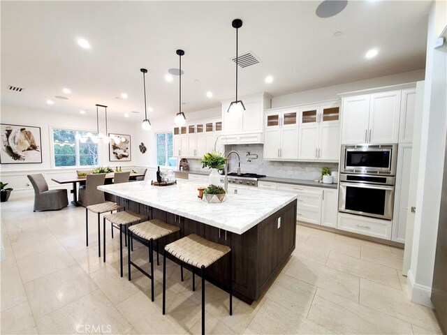 kitchen with appliances with stainless steel finishes, decorative light fixtures, white cabinetry, decorative backsplash, and a large island with sink