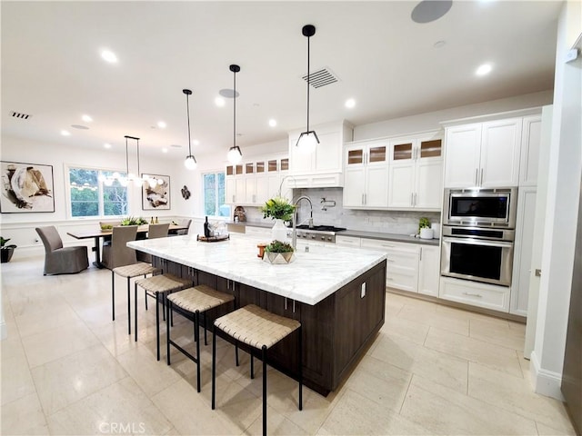 kitchen featuring appliances with stainless steel finishes, tasteful backsplash, white cabinets, a large island with sink, and hanging light fixtures