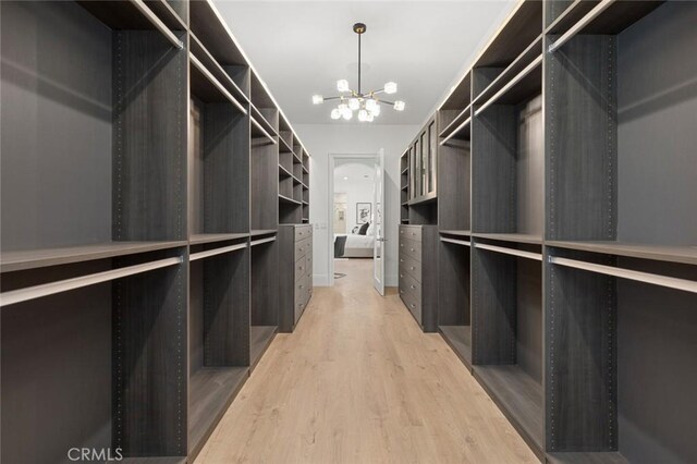 spacious closet featuring light hardwood / wood-style floors and a chandelier