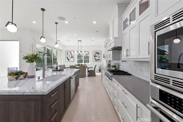 kitchen featuring sink, a kitchen island with sink, hanging light fixtures, dark brown cabinets, and stainless steel appliances