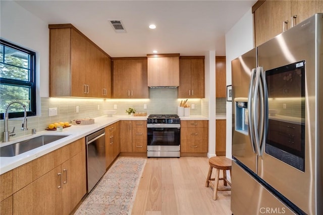 kitchen with appliances with stainless steel finishes, sink, decorative backsplash, wall chimney exhaust hood, and light hardwood / wood-style flooring