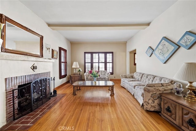 living room with a brick fireplace, beam ceiling, and light wood-type flooring