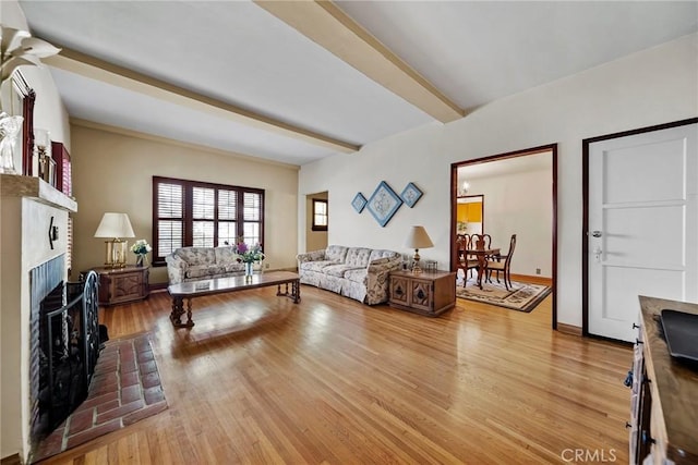 living room with beamed ceiling, a brick fireplace, and light wood-type flooring