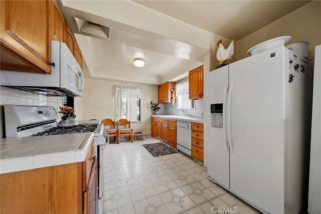 kitchen with sink, tile counters, white appliances, and decorative backsplash