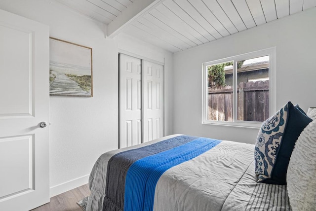 bedroom with beamed ceiling, wood ceiling, hardwood / wood-style floors, and a closet