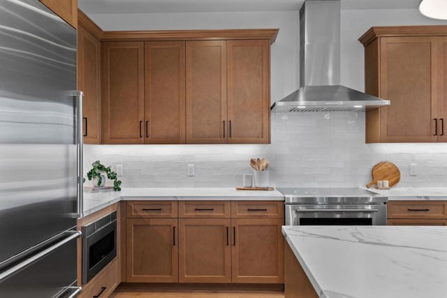 kitchen featuring built in appliances, light stone counters, tasteful backsplash, and wall chimney exhaust hood