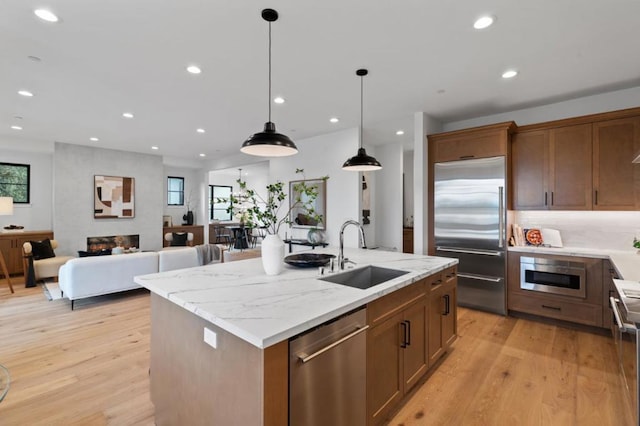 kitchen with sink, decorative light fixtures, an island with sink, stainless steel appliances, and light stone countertops