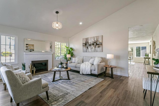 living room with wood-type flooring, a brick fireplace, a wealth of natural light, and high vaulted ceiling