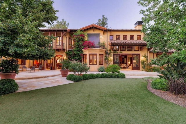 back house at dusk featuring a yard, a patio area, and a balcony