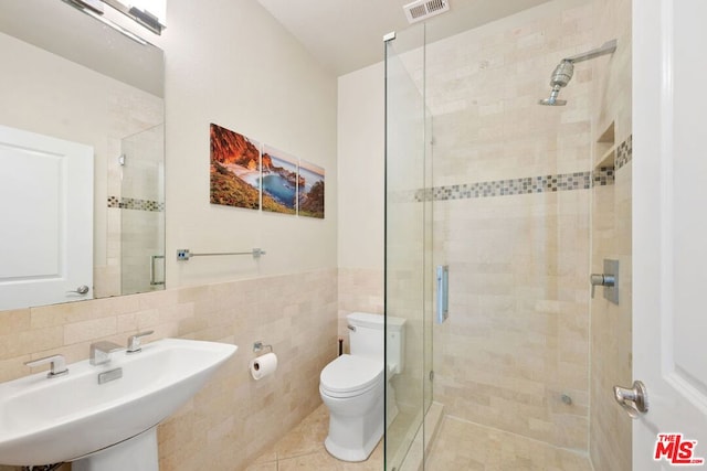 bathroom with toilet, sink, tile walls, a shower with door, and tile patterned flooring